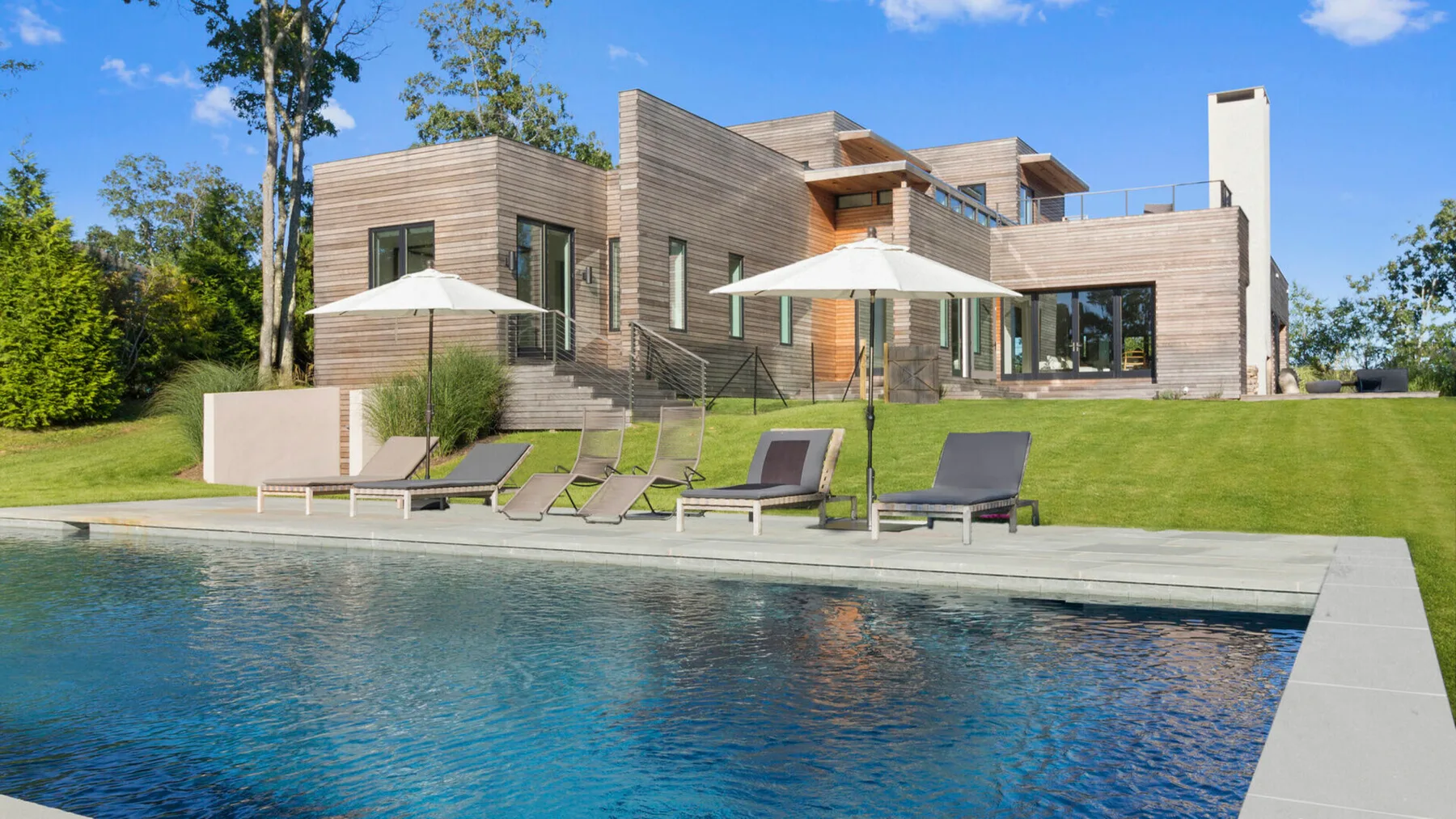 Una casa moderna da a una piscina con asientos reclinables y sombrillas.
