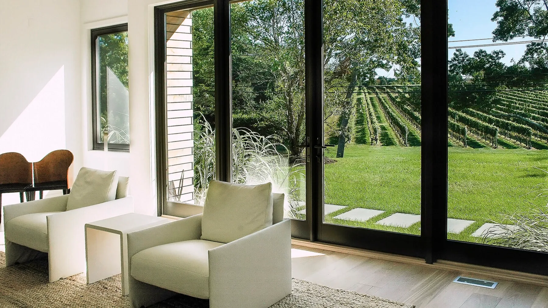 Una luminosa sala de estar con asientos junto a grandes ventanas, con vistas al césped y a las hileras de plantas.