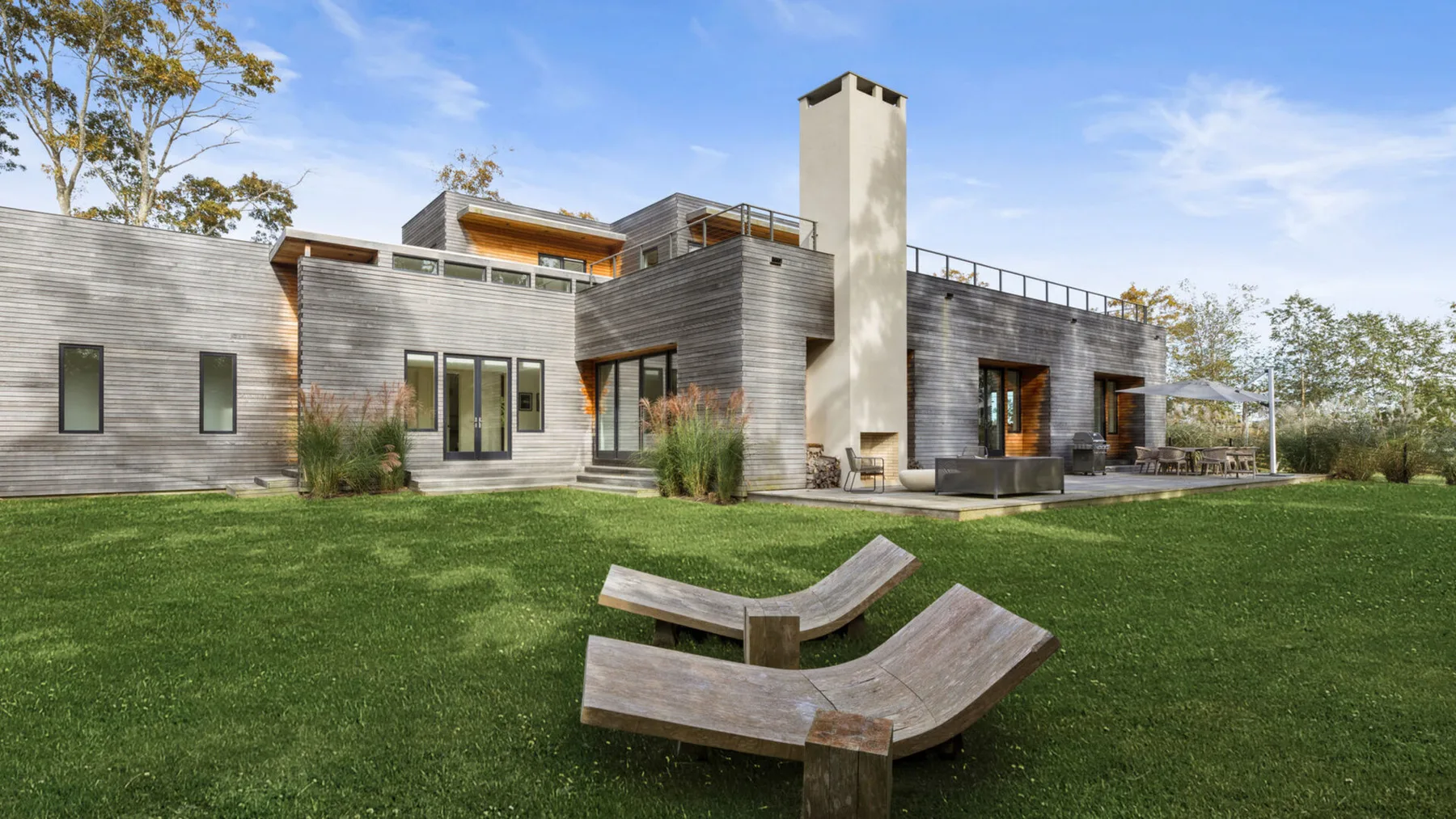 Una casa moderna con un amplio césped y asientos curvos al aire libre.