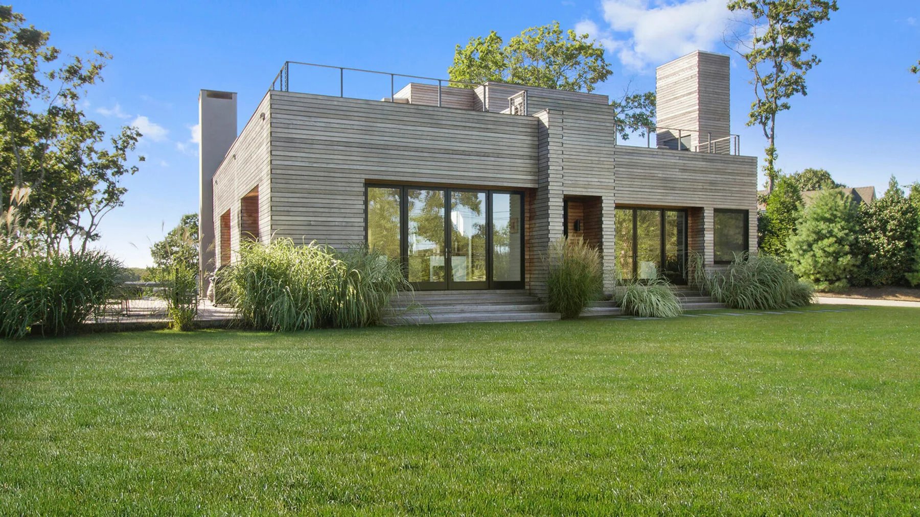 Una casa moderna con grandes ventanas se alza junto a un amplio césped verde.