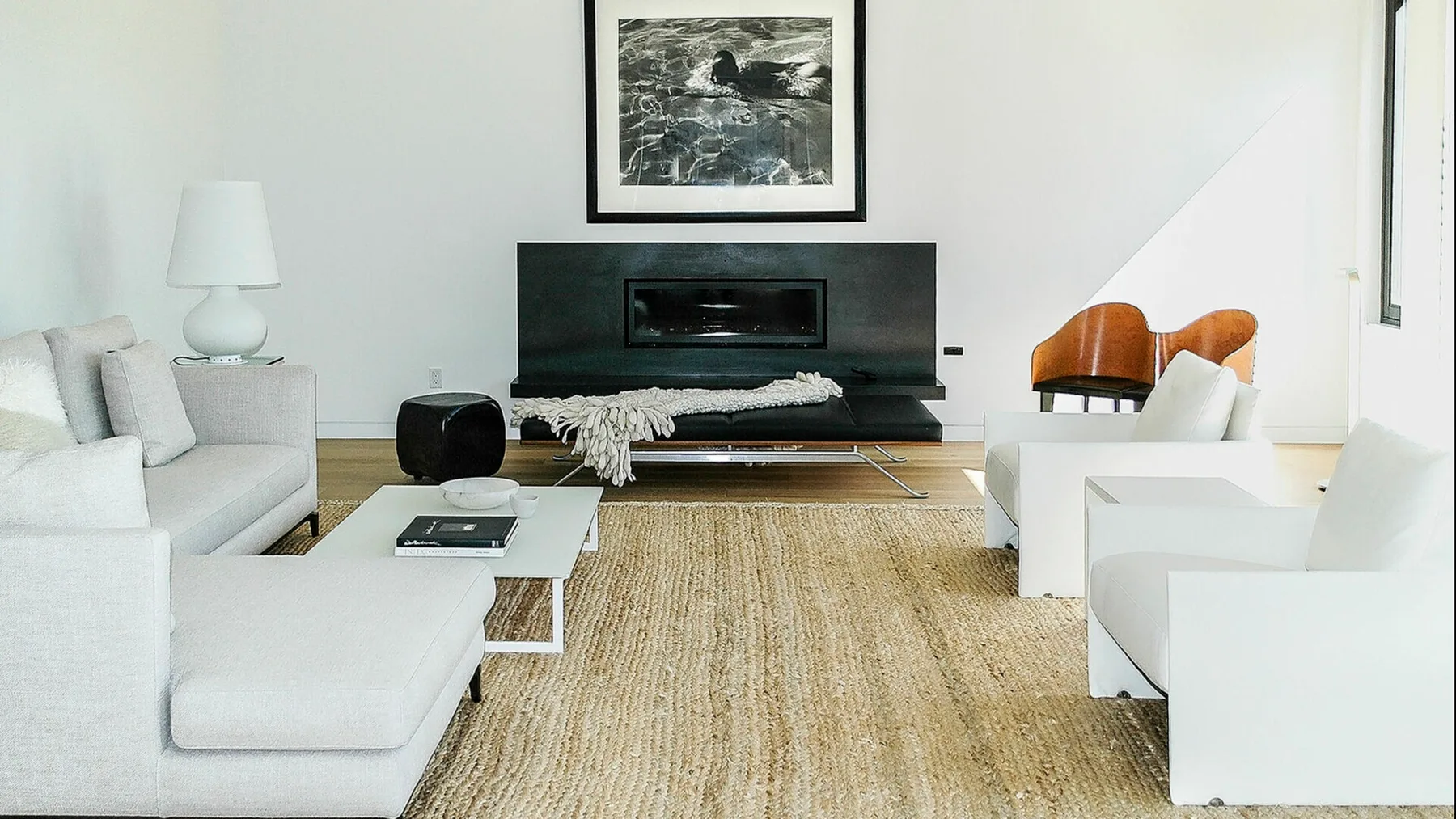 Una sala de estar moderna con asientos blancos, una mesa de centro baja y una chimenea oscura.
