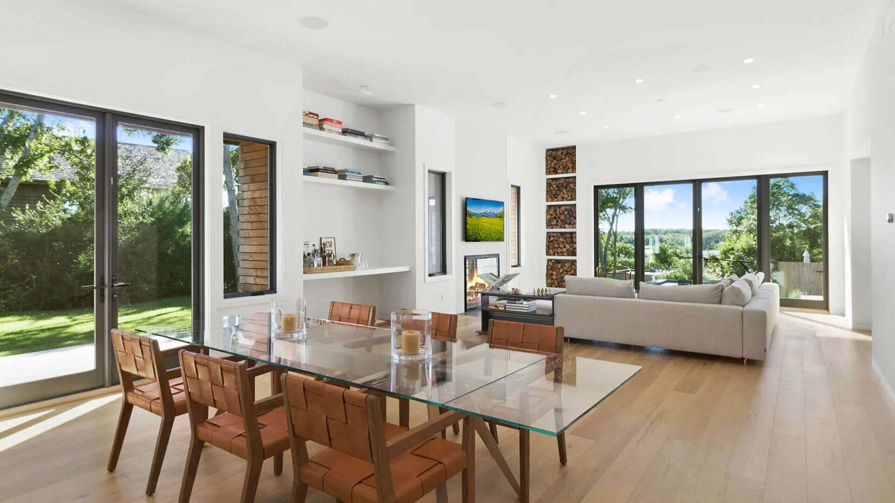 Un luminoso salón-comedor de planta abierta con grandes ventanas y una mesa de comedor de vidrio.