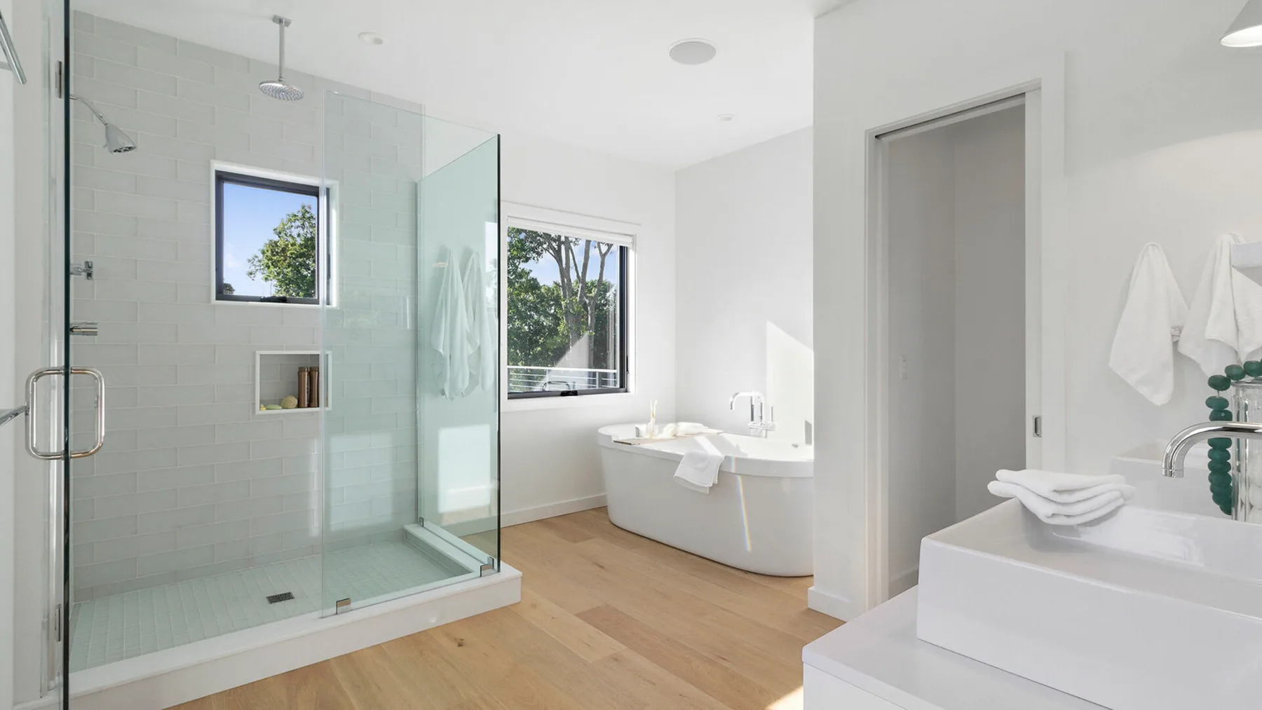 Un baño luminoso con una ducha de vidrio y una bañera junto a una ventana.