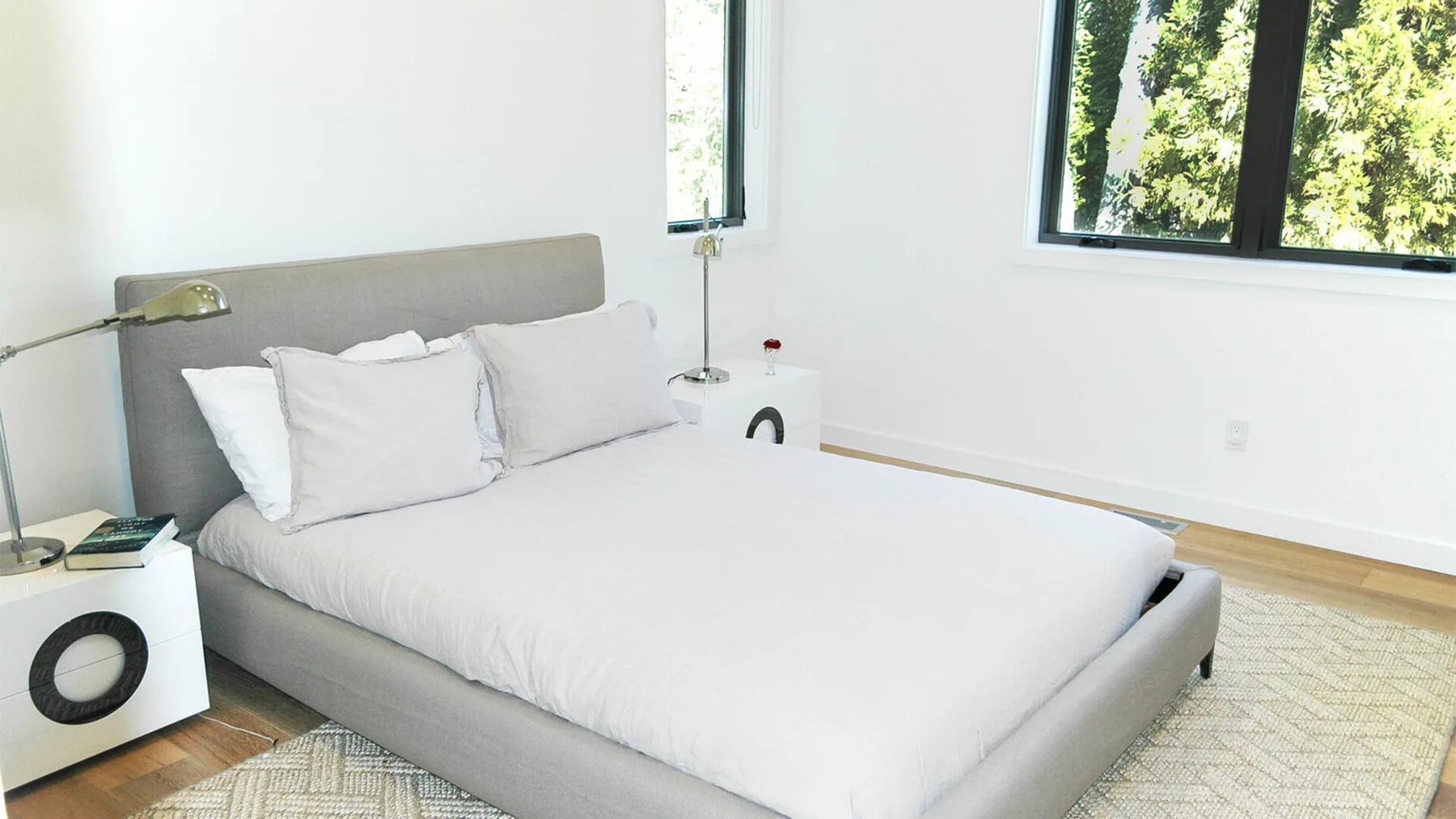 Un dormitorio luminoso con una cama bien arreglada y grandes ventanas.