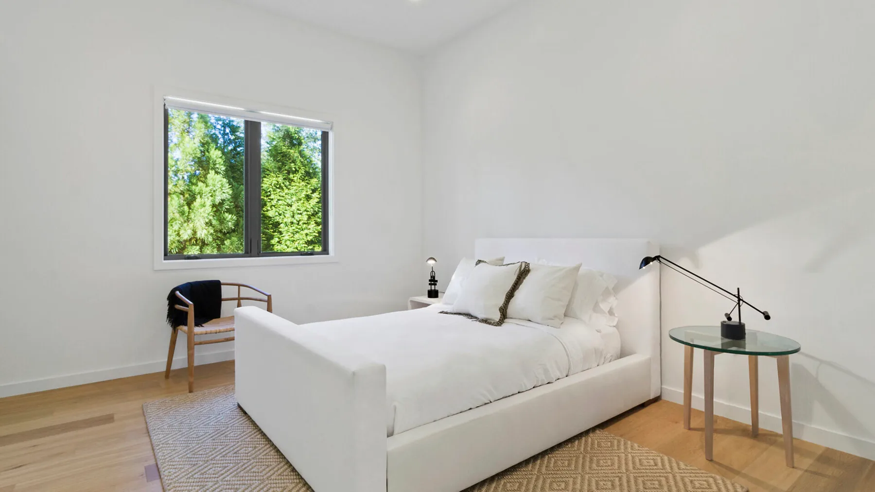 Un dormitorio luminoso con una cama blanca junto a una ventana grande.
