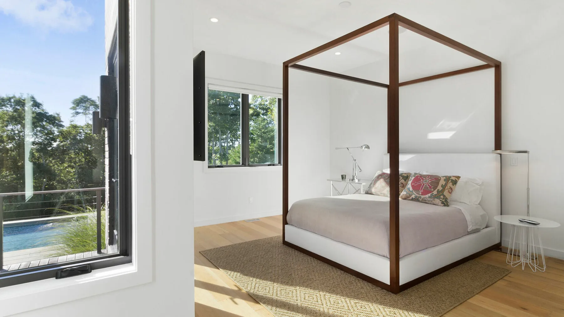 Un dormitorio luminoso con una cama con dosel y una gran ventana con vistas a una piscina.