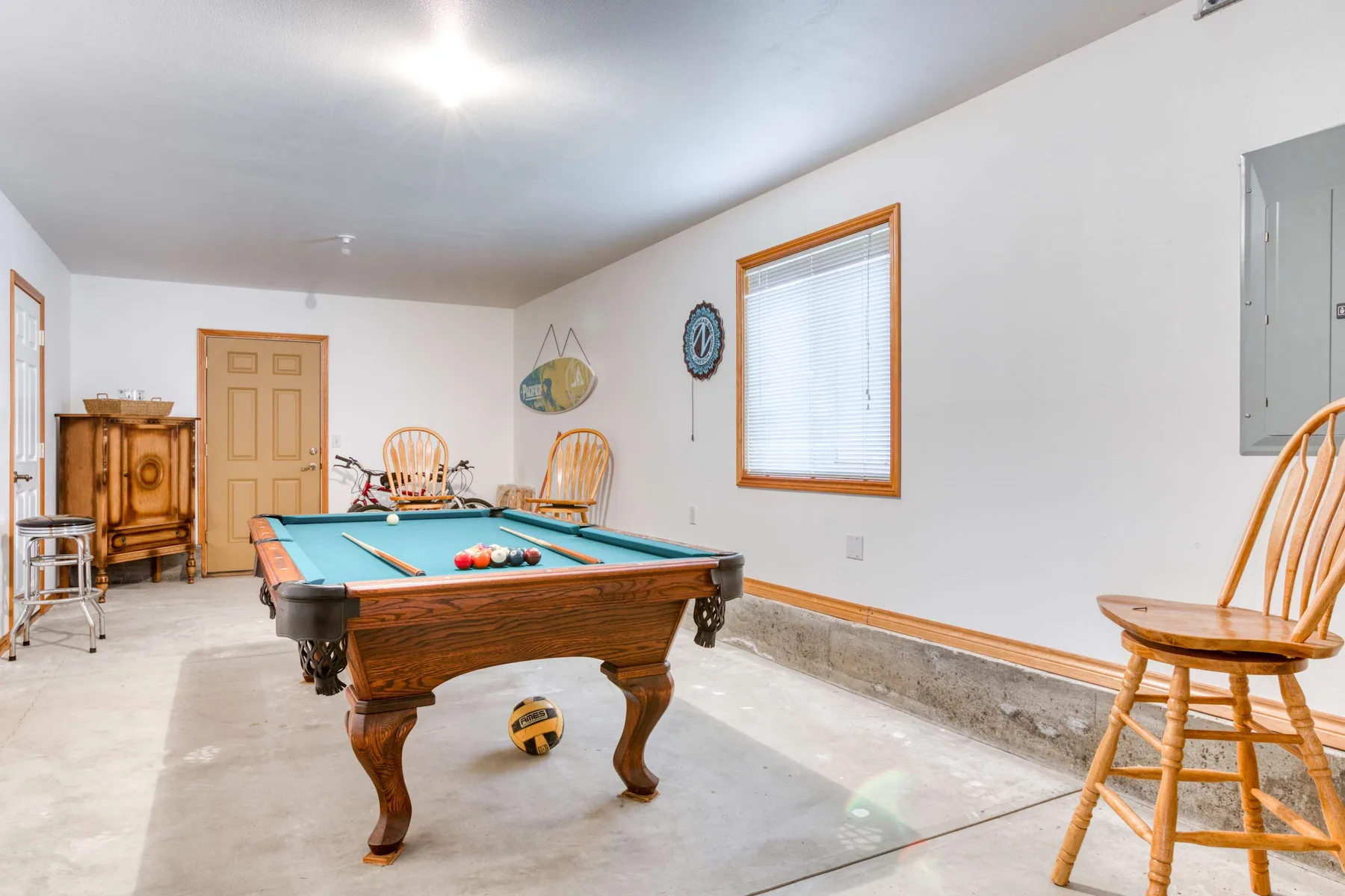 A basement game room with a pool table and wooden chairs.