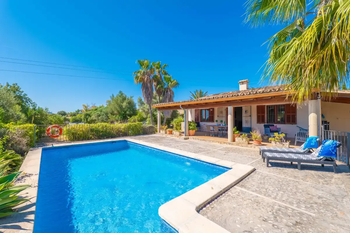 Una piscina exterior está junto a una casa de una planta con patio cubierto.
