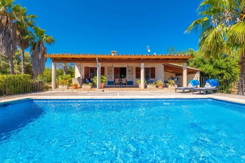 Una piscina está frente a una casa de una planta con un patio cubierto.