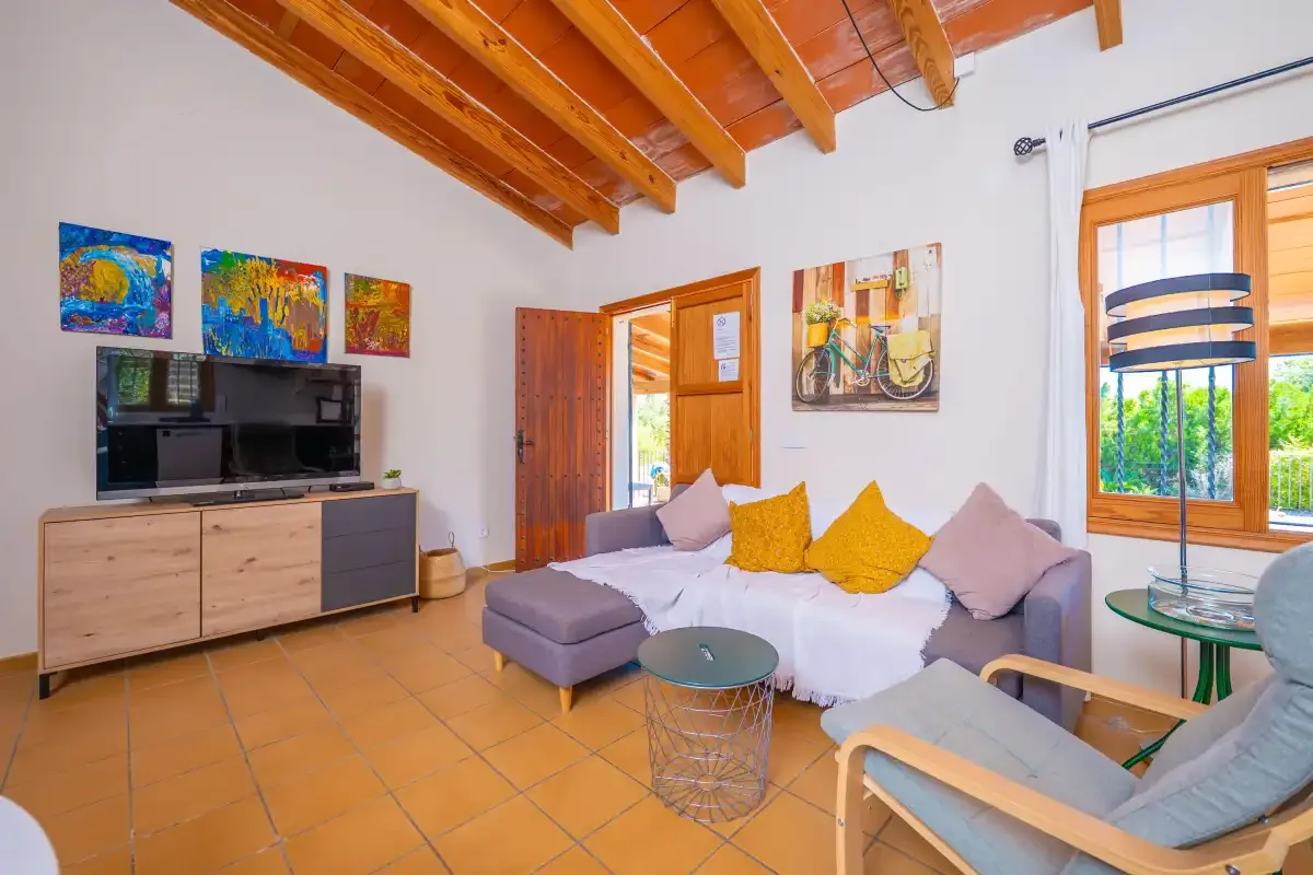 Una sala de estar con zona de asientos, televisor y vigas de madera a la vista.
