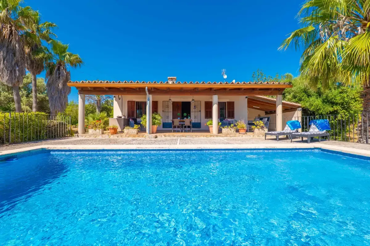 Una piscina frente a una casa de una planta, rodeada de palmeras.