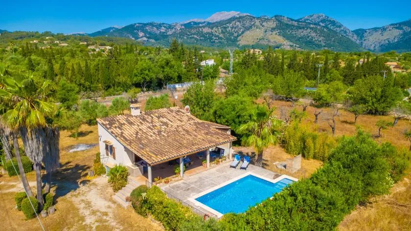 Vista aérea de una casa con piscina entre la vegetación y montañas a lo lejos.