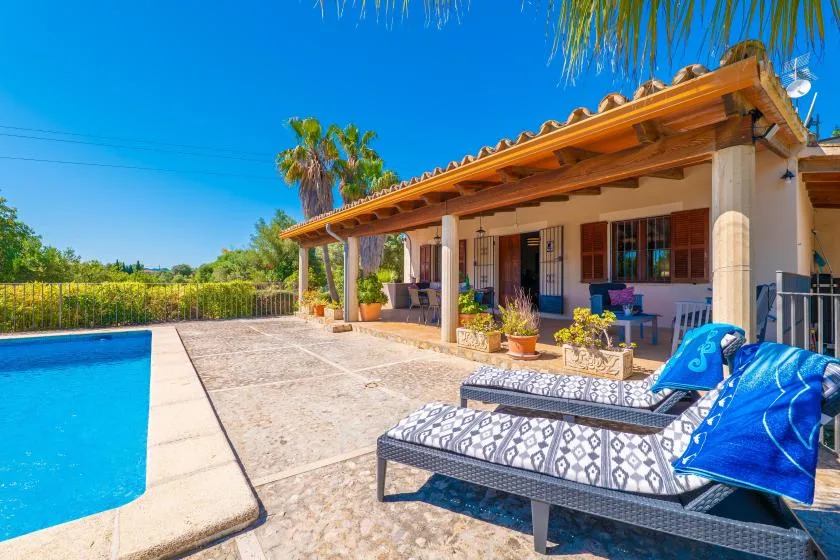 Un patio soleado junto a la piscina, con tumbonas y una terraza cubierta.