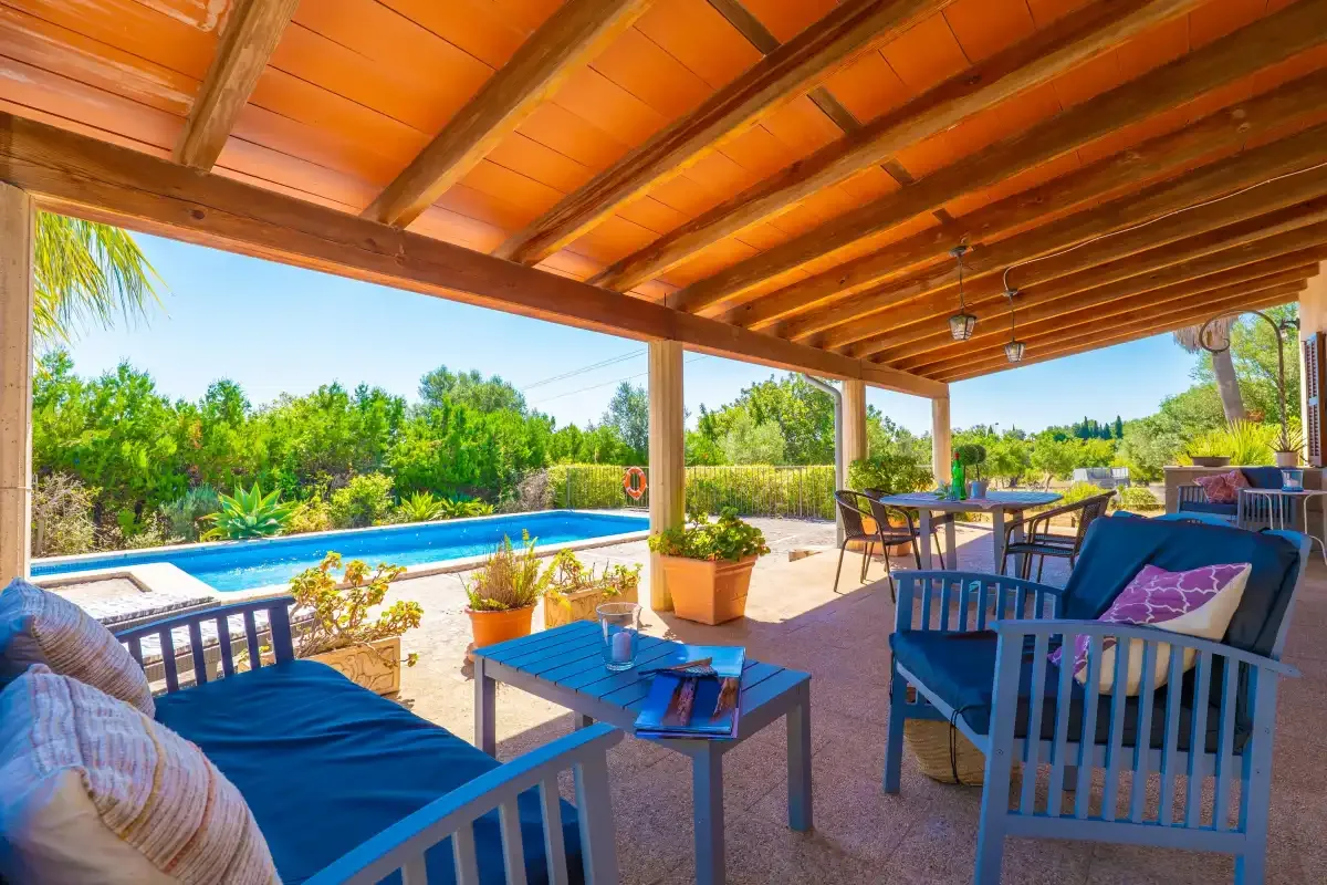 Un patio exterior cubierto con asientos y una piscina cercana.