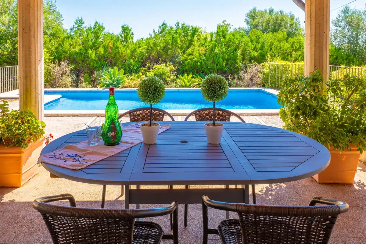 Una zona de comedor en un patio sombreado da a una piscina y vegetación.
