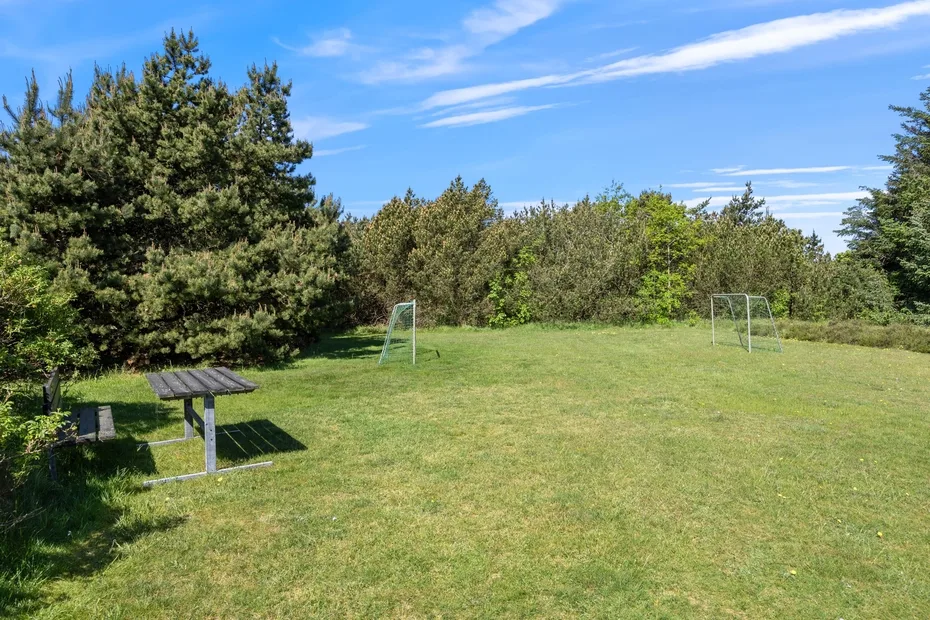 Un campo de césped rodeado de árboles, con pequeñas porterías y una mesa de picnic.