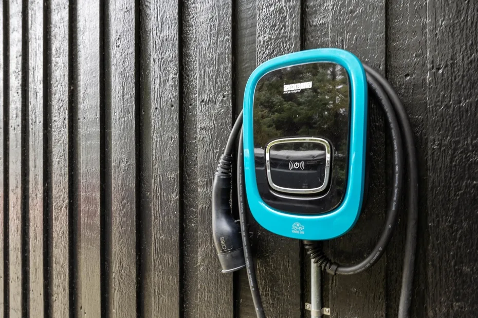 Una unidad de carga para vehículos eléctricos está montada en una pared oscura de madera vertical.