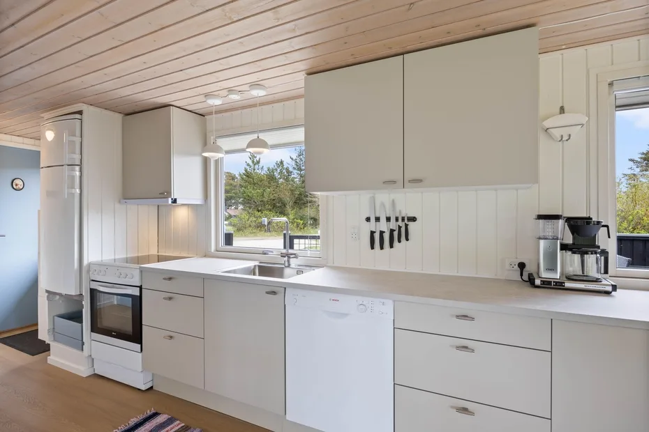Una cocina luminosa con gabinetes blancos, una encimera y una ventana con vista a la vegetación.