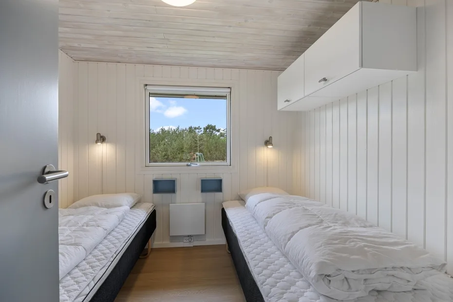 Un dormitorio luminoso con dos camas bajo una ventana que da a los árboles.