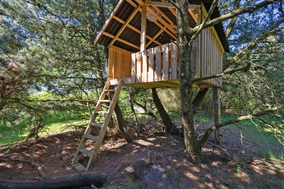 Una casa de árbol de madera se alza entre los árboles, con una escalera de acceso.