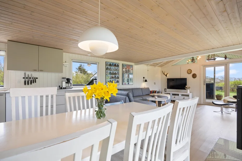 Un comedor y sala de estar diáfanos y luminosos tienen una mesa larga y grandes ventanas.