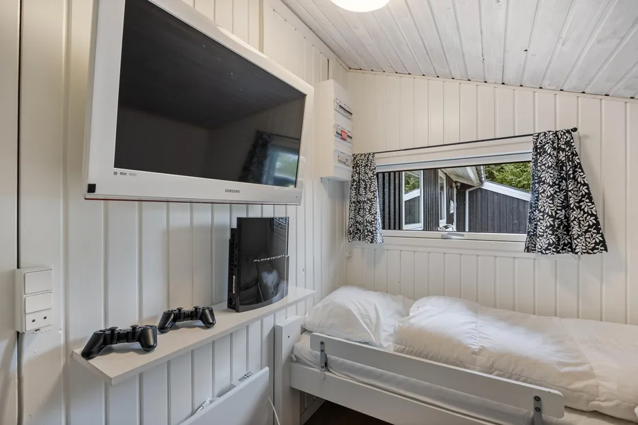 Un dormitorio con una cama bajo una ventana y un televisor en la pared.