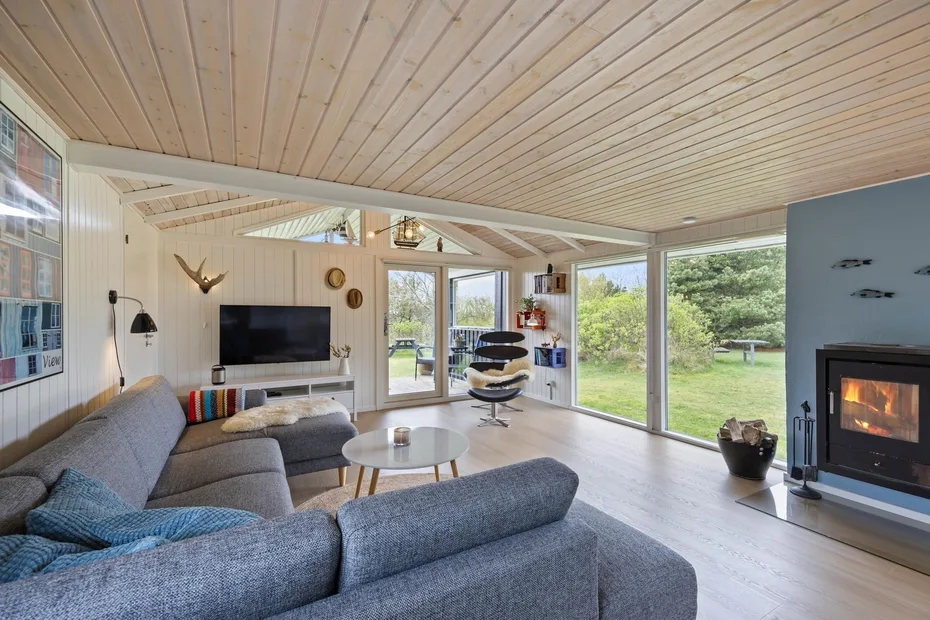 Sala de estar con asientos, un televisor y ventanales con vistas al jardín.