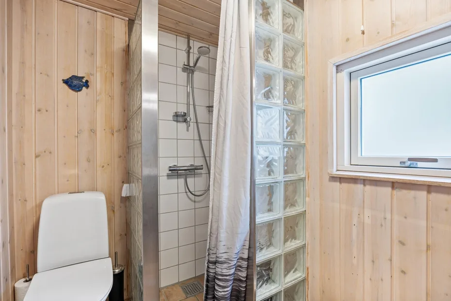 Un baño con ducha de azulejos, pared de bloques de vidrio y ventana.