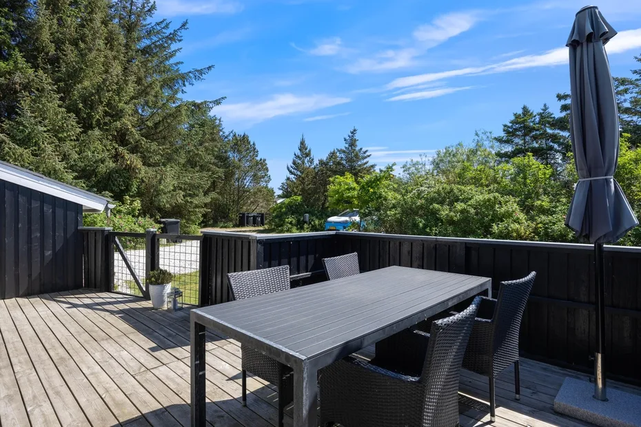 Comedor al aire libre con una mesa y sillas sobre una terraza de madera.