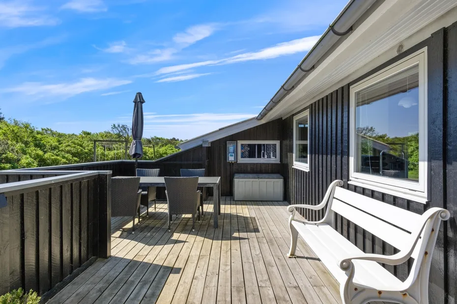 Una terraza de madera con asientos al aire libre y un banco blanco junto a la casa.