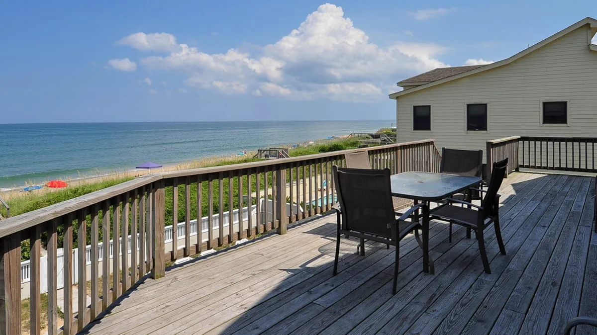 A wooden deck overlooks the ocean, with outdoor seating beside the railing.