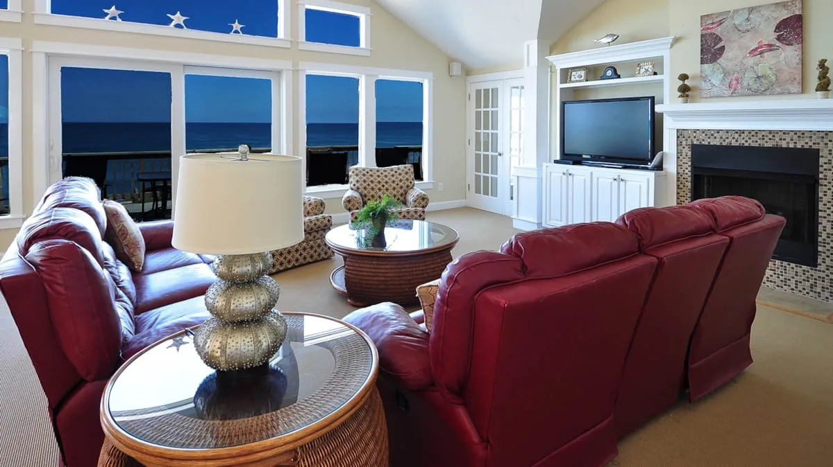 A living room with red seating, a fireplace, and large windows overlooking the water.