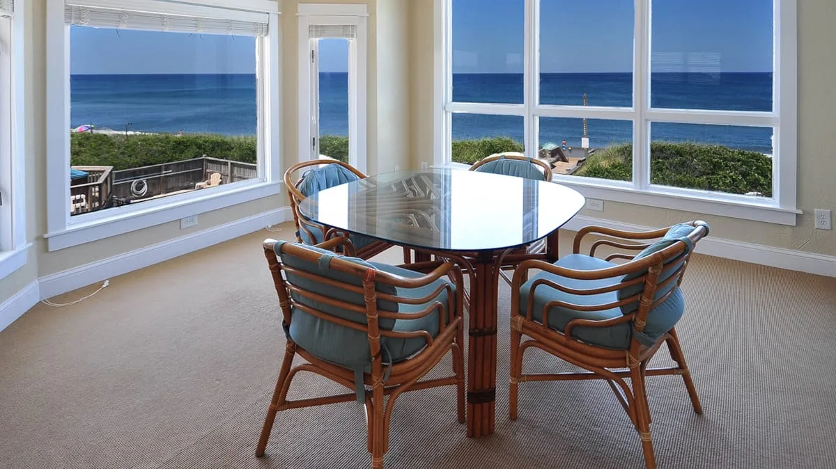 A dining table and chairs sit beside windows overlooking the ocean.