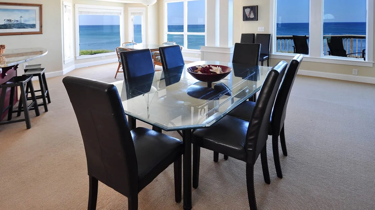 A dining area with a glass table and large windows overlooking the ocean.