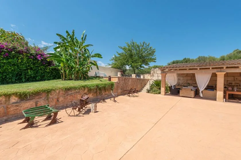 Un patio soleado pavimentado con asientos de jardín y una zona de comedor exterior a la sombra.