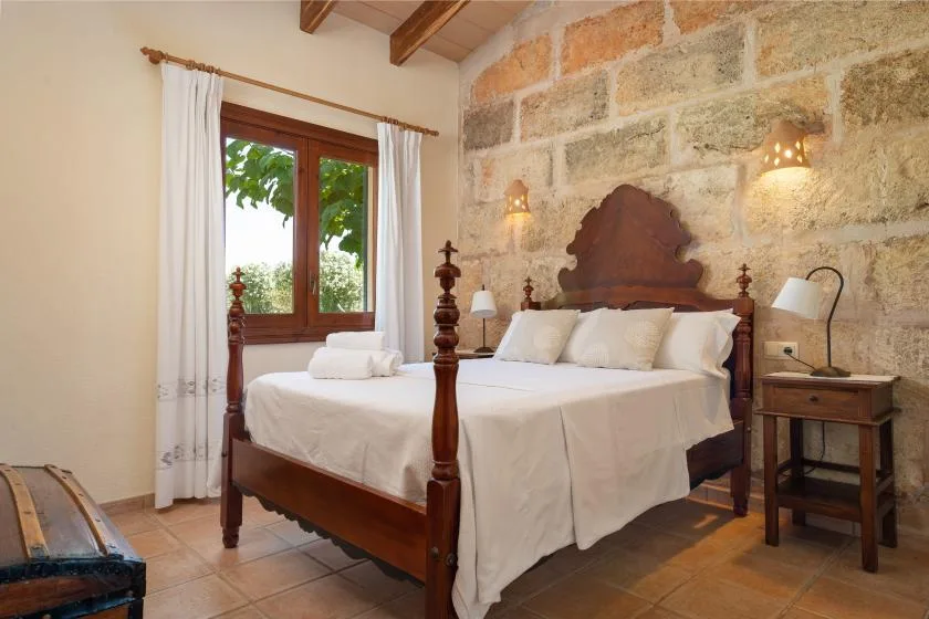 Un dormitorio con una cama de madera, ropa de cama blanca y una ventana con cortinas.