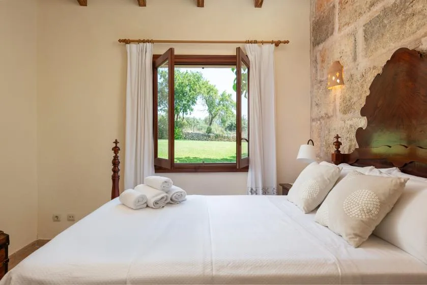 Un dormitorio con una cama bien hecha junto a una ventana abierta con vistas a la vegetación.