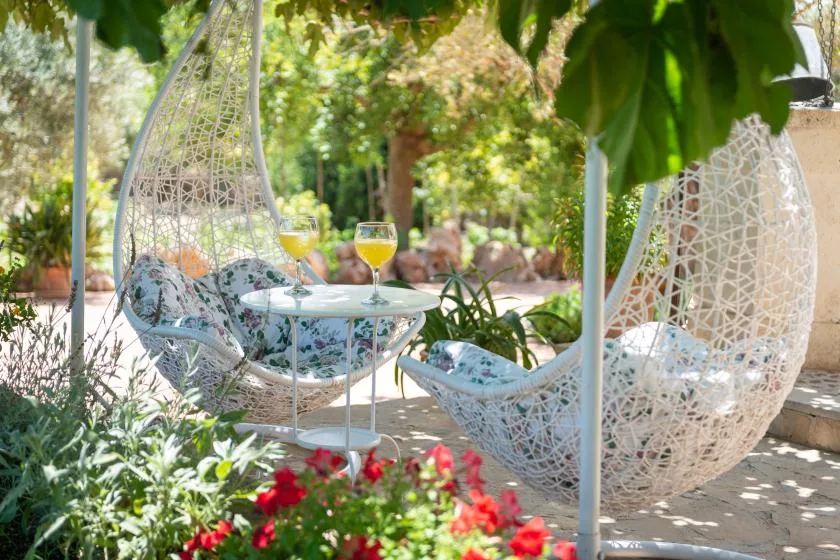 Una zona de estar en el jardín, con asientos colgantes alrededor de una mesa entre flores y plantas.