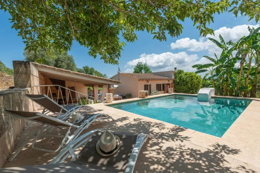 Una piscina exterior junto a una casa, con tumbonas en el patio.