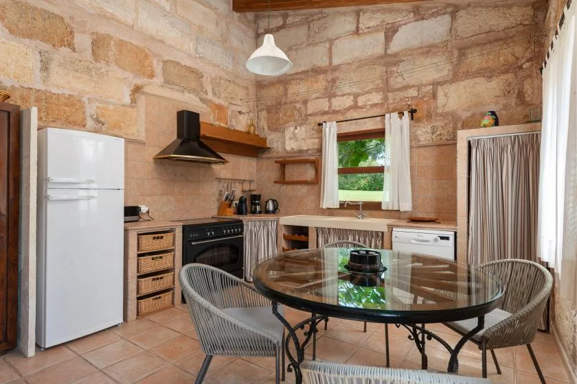 Una cocina rústica con comedor, mesa de cristal y paredes de piedra vista.