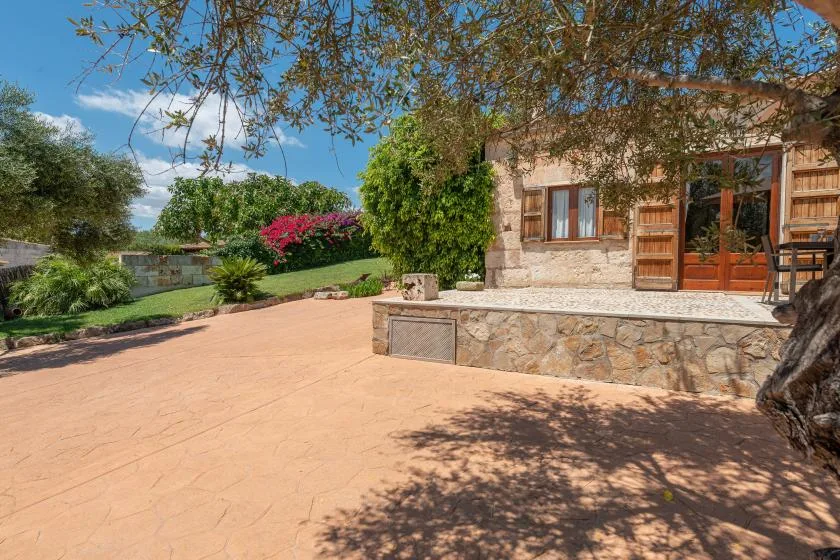Una casa de piedra da a un amplio patio pavimentado junto a un jardín cuidado.