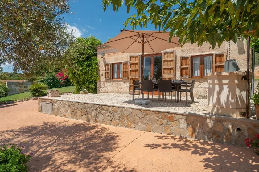 Un patio soleado con una mesa y sillas junto a una casa de piedra.