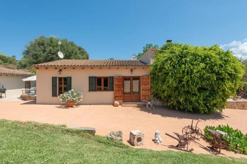 Una casa de una planta con techo de tejas da a un patio soleado y un jardín.