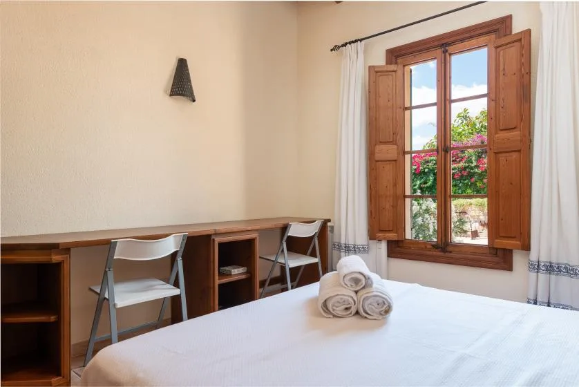 Un dormitorio con una cama, un escritorio y una ventana con vistas a vegetación.