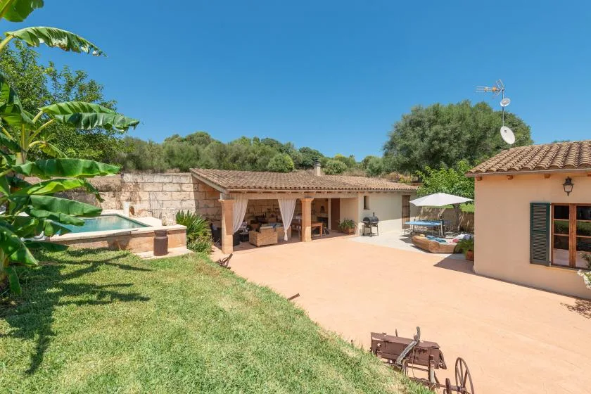Un patio soleado con una terraza cubierta y una piscina.