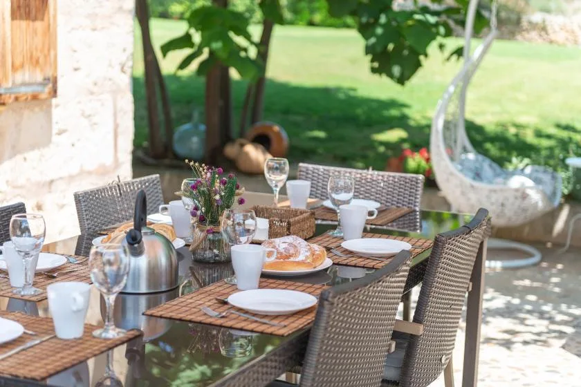 Una mesa de comedor al aire libre está puesta con platos y bebidas junto a un jardín.