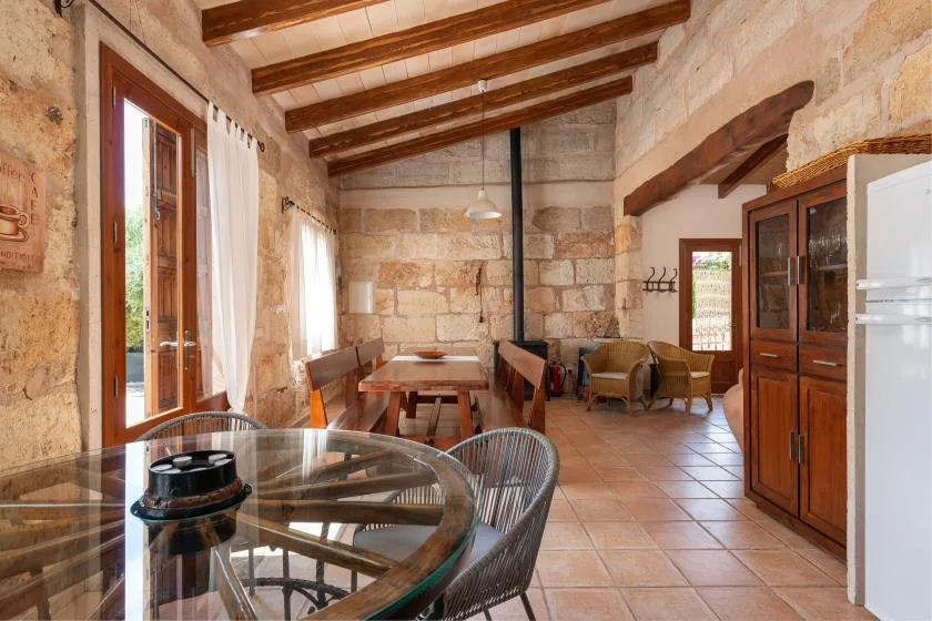 Comedor de paredes de piedra, con mesas de madera y una mesa de vidrio en primer plano.