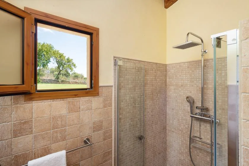 Un baño con azulejos, una ducha de vidrio y una ventana con marco de madera.