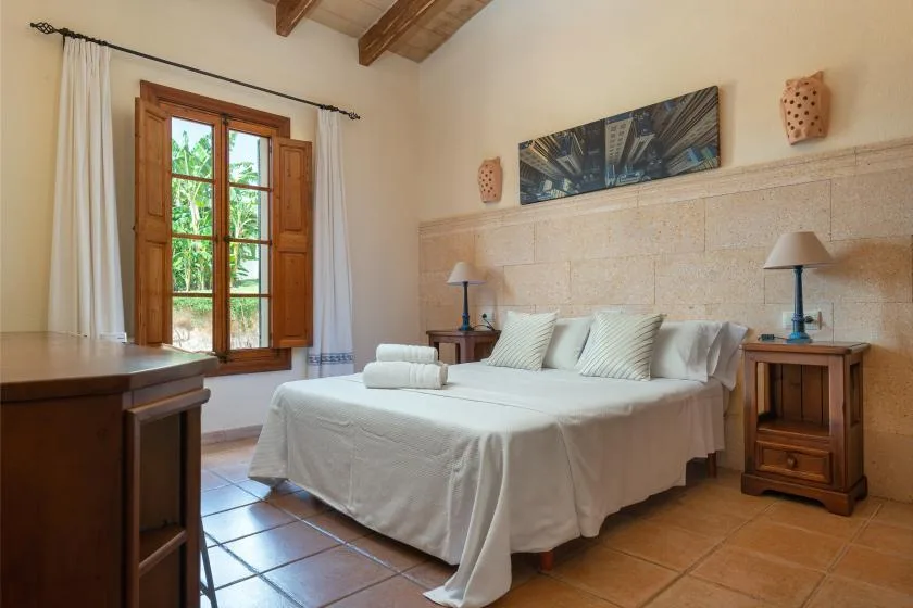 Un dormitorio con una cama tendida, mesitas de noche y una ventana.