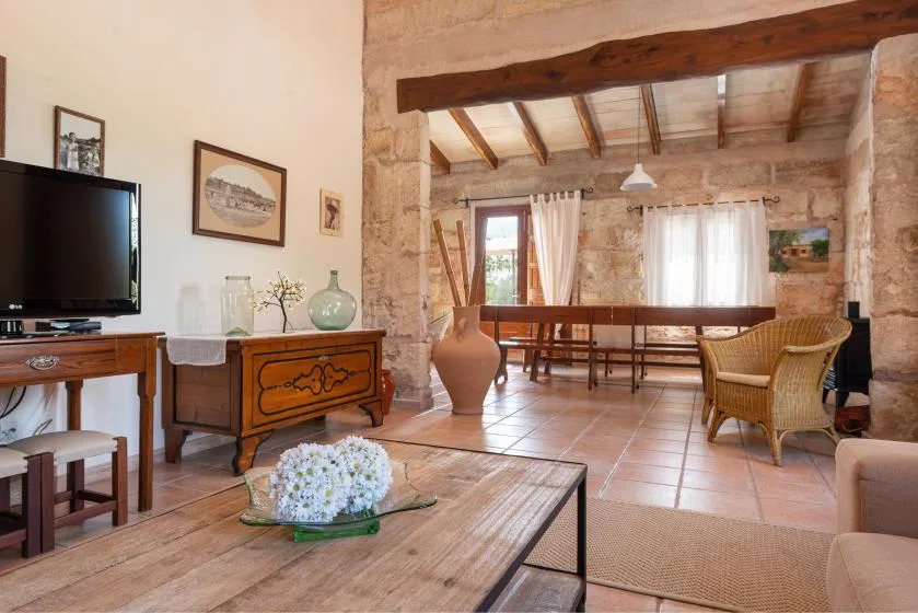 Sala de estar y comedor rústicos con muebles de madera, vigas expuestas y una pared de piedra.